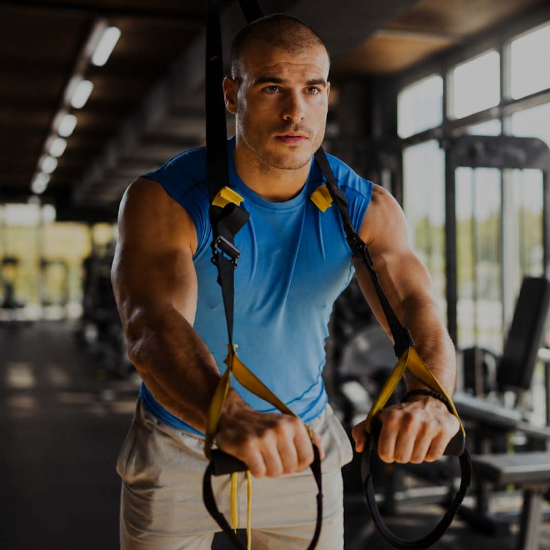 Muscular athlete performing TRX suspension training in modern gym