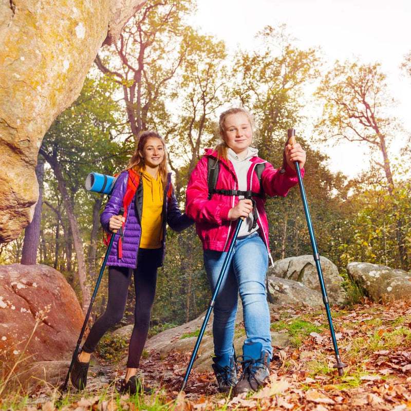 two girls hiking forest trail with trekking poles and backpacks
